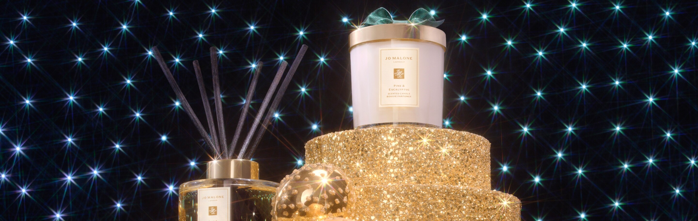 pine & eucalyptus home candle & diffuser on glittering gold plinths with spotlights behind